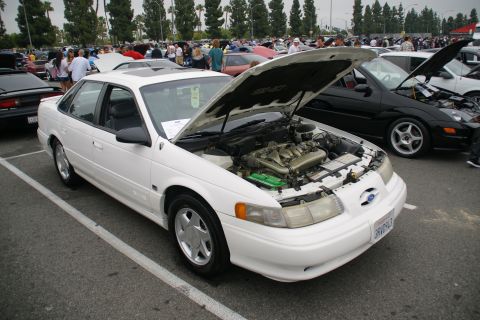 1993 Ford Taurus - A white 1993 Ford Taurus is displayed with its hood open, revealing the engine compartment, at an outdoor car show.