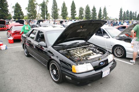 1993 Ford Taurus - A black 1993 Ford Taurus SHO is displayed with its hood open, revealing the engine, at a car show.