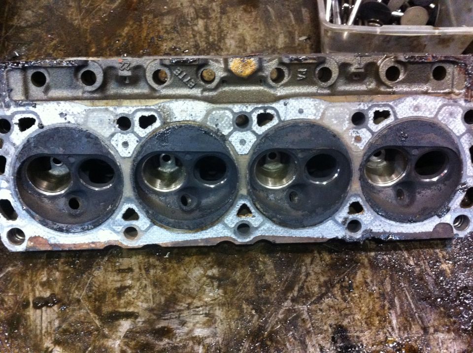 Used engine cylinder head with four combustion chambers visible. Text '8118' is cast into the metal