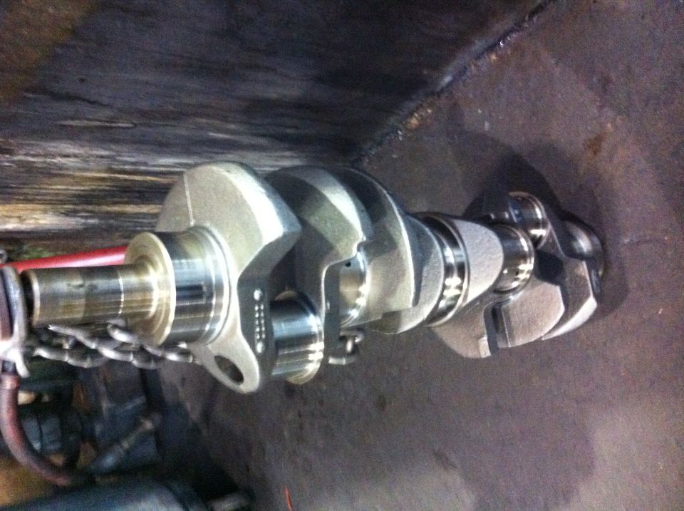 Metal crankshaft with visible counterweights and journals, resting on a dark surface