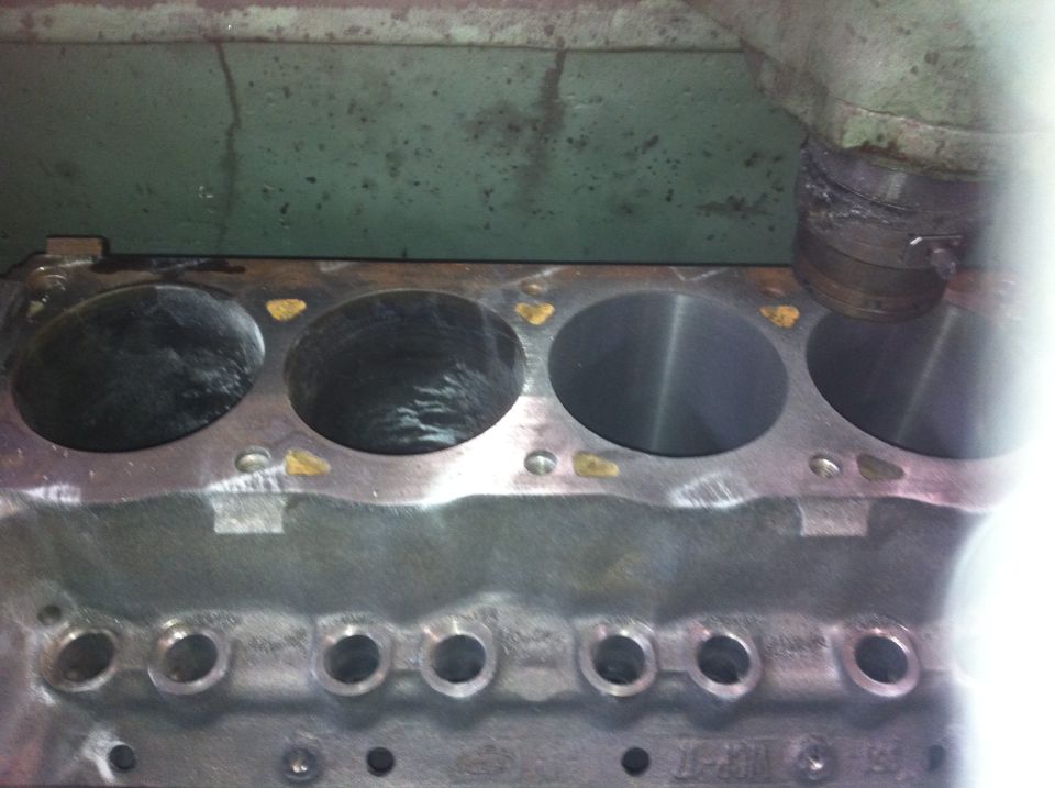 Close-up of engine block cylinders, some showing wear. A machine is visible at the top right