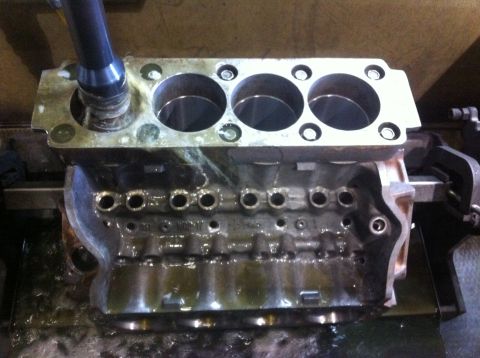 1990 Ford Bronco - disassembled V6 engine block sits on a shop bench, deck surface up, showing three open cylinder bores and head bolt holes.
