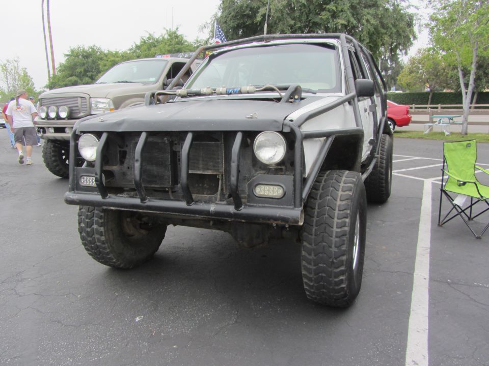 Modified SUV with a roll cage and off-road tires parked next to a pickup truck