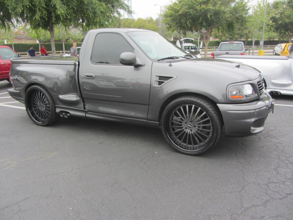 Gray pickup truck with custom rims and lowered suspension, viewed from the front three-quarter angle