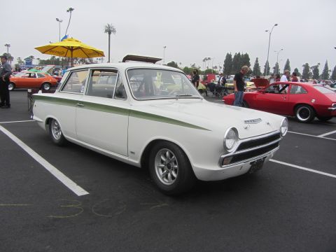 1964 Ford Ranchero - A white sedan with green racing stripes is parked in a lot next to other vehicles.