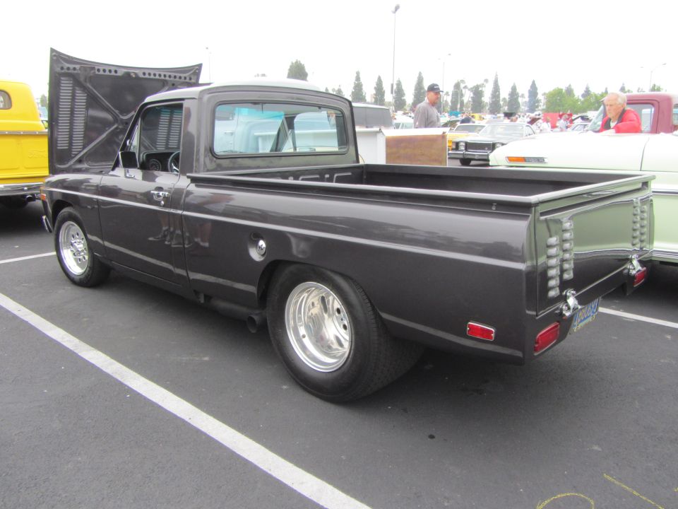 Dark gray pickup truck with hood up, parked next to a yellow truck and a white car