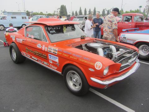 1964 Ford Ranchero - A modified Ford Mustang drag car is parked at an outdoor event, with its engine exposed.