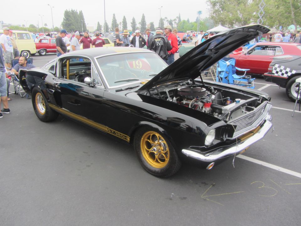 Black 1966 Ford Mustang Shelby GT350 with gold stripes and wheels, hood open