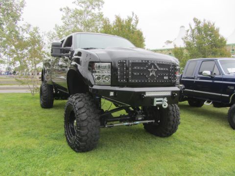 1964 Ford Ranchero - Modified black Ford F-series truck with large tires and custom front end, parked beside a blue Ford Bronco.