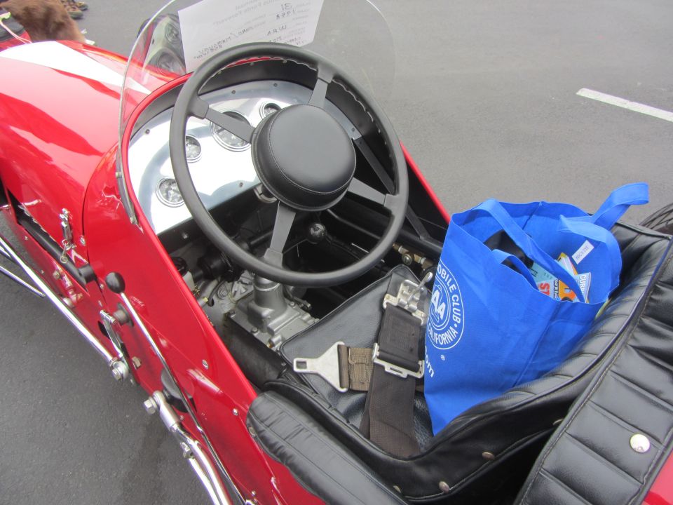 Red race car interior with black steering wheel, gauges, seatbelt, and blue tote bag