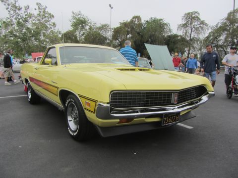 1964 Ford Ranchero - This yellow Ford Ranchero features a distinctive side stripe and hood scoop, parked at an outdoor event.