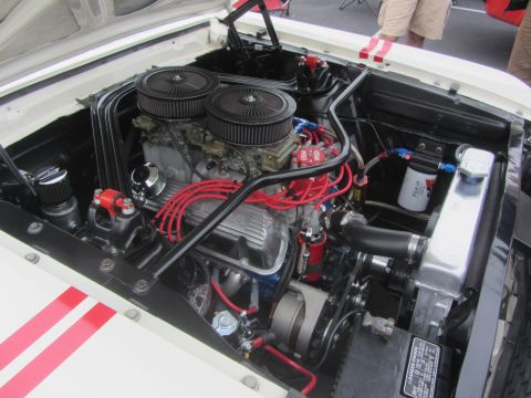 1964 Ford Ranchero - The engine bay of a white 1964 Ford Ranchero, a V8 engine with performance upgrades and red racing stripes on the fender.
