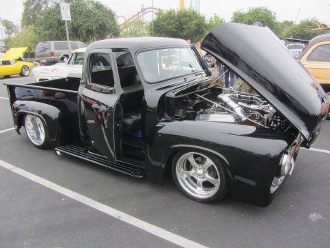 1964 Ford Ranchero - This black Ford F-100 pickup truck features custom wheels and an open hood revealing its engine.