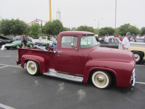 1964 Ford Ranchero - This red pickup truck is parked at an outdoor car show with other vehicles and attendees.