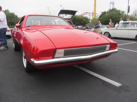 1964 Ford Ranchero - Front view of a red coupe with a distinctive chrome grille, parked in a lot with other vehicles.