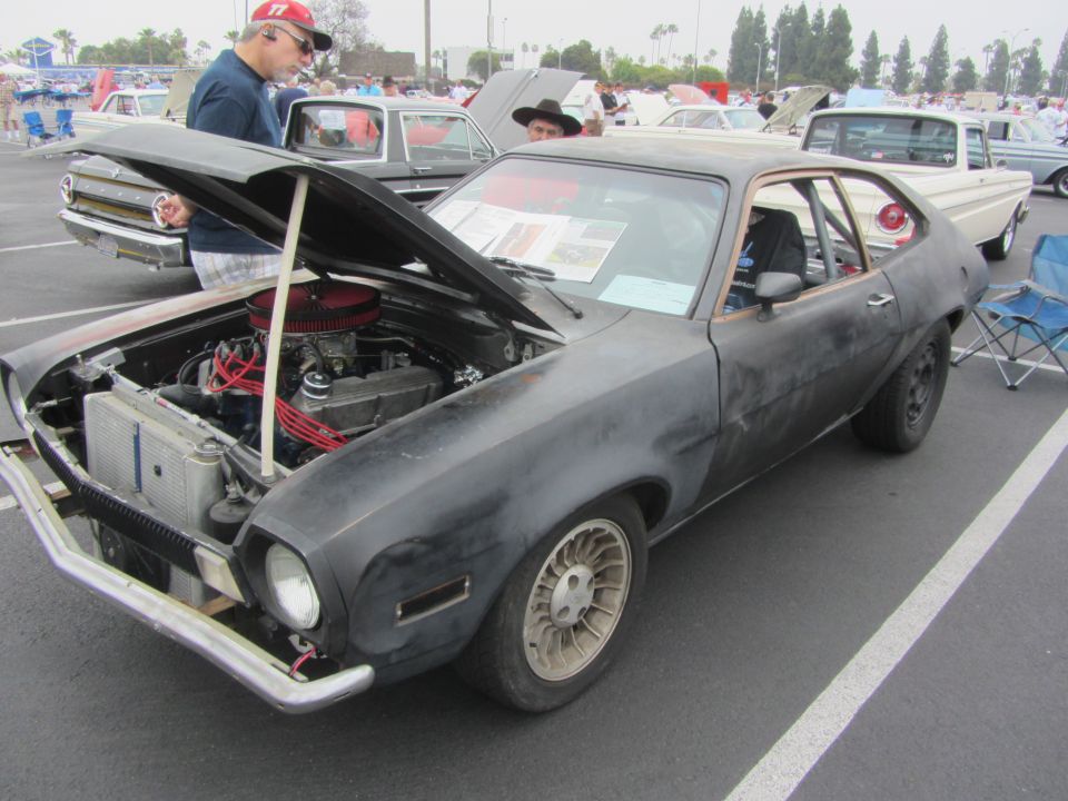 Black Ford Pinto with hood open, showing engine. Other cars and people in background