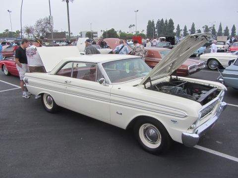 1964 Ford Ranchero - A white 1963 Ford Falcon coupe is displayed with its hood open at a car show, surrounded by other vehicles.