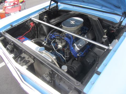 1964 Ford Ranchero - The engine bay of a blue 1964 Ford Falcon shows a V8 engine with aftermarket chrome components and blue spark plug wires.