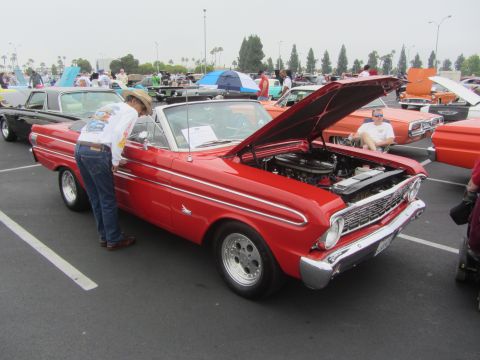 1964 Ford Ranchero - A man inspects a red 1964 Ford Ranchero convertible at an outdoor car show.