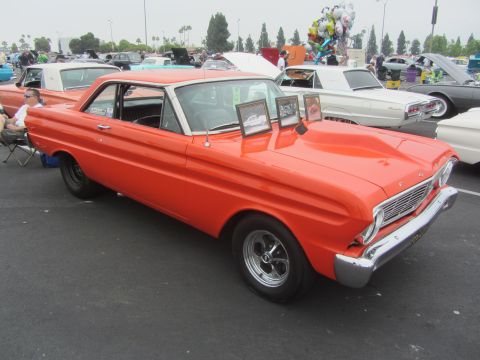 1964 Ford Ranchero - An orange 1964 Ford Ranchero with a white roof and hood scoop is parked at an outdoor event.