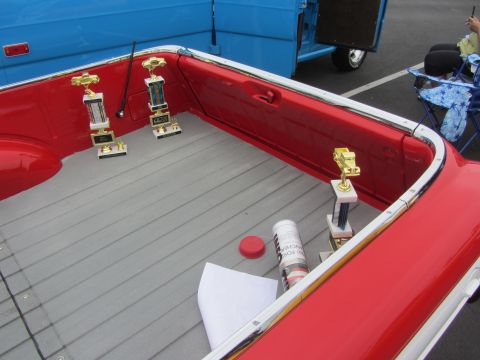 1964 Ford Ranchero - The bed of a red pickup truck is shown with several trophies inside, next to a blue truck.