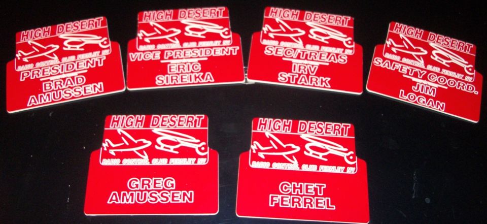 Red name tags with white text and graphics of a plane and helicopter. Text includes 'HIGH DESERT', titles, and names