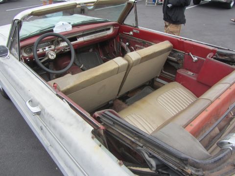 1964 Ford Ranchero - The interior of a vintage convertible shows worn tan seats and red door panels, with the steering wheel and dashboard in view.