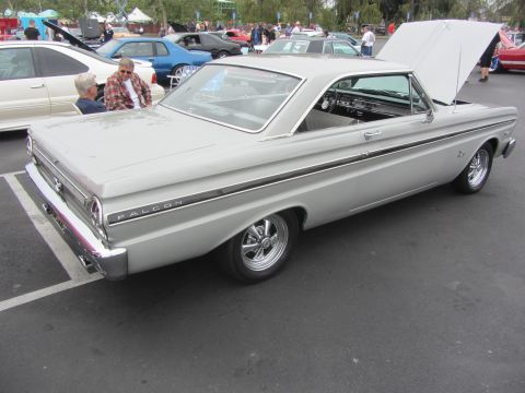 1964 Ford Ranchero - A silver 1964 Ford Falcon coupe is viewed from the rear three-quarter angle with its hood up at an outdoor car show.