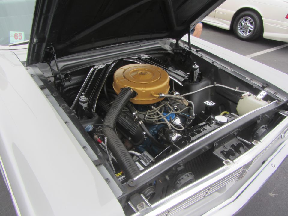 Engine bay with gold air cleaner and a '65 sticker on the windshield
