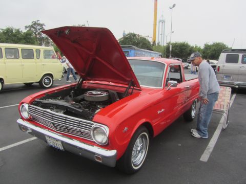 1964 Ford Ranchero - A man inspects a red 1964 Ford Ranchero parked with its hood open, revealing the engine bay.