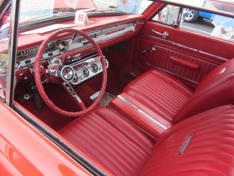 1964 Ford Ranchero - The interior of a classic red car features a detailed dashboard and plush seating.