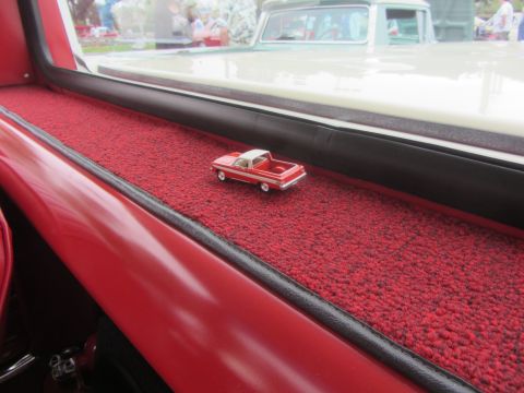 1964 Ford Ranchero - A miniature red and white pickup truck sits on the red carpeted dashboard of a classic car.