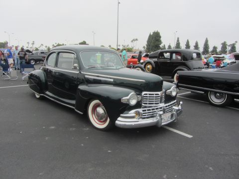 1964 Ford Ranchero - A vintage dark green sedan with whitewall tires is parked at an outdoor event with other cars.