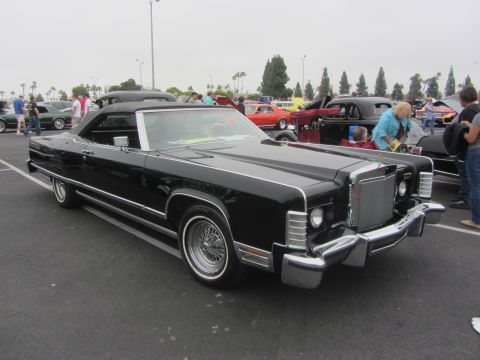 1964 Ford Ranchero - A black convertible with distinctive chrome accents and wire wheels is parked at an outdoor event.