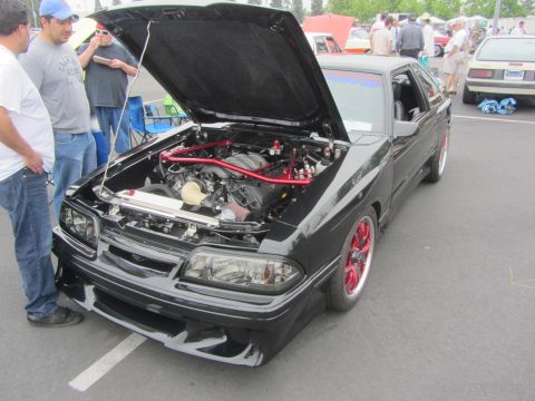 1964 Ford Ranchero - A black car with its hood open, revealing the engine and red-accented chassis, is parked at an outdoor event.