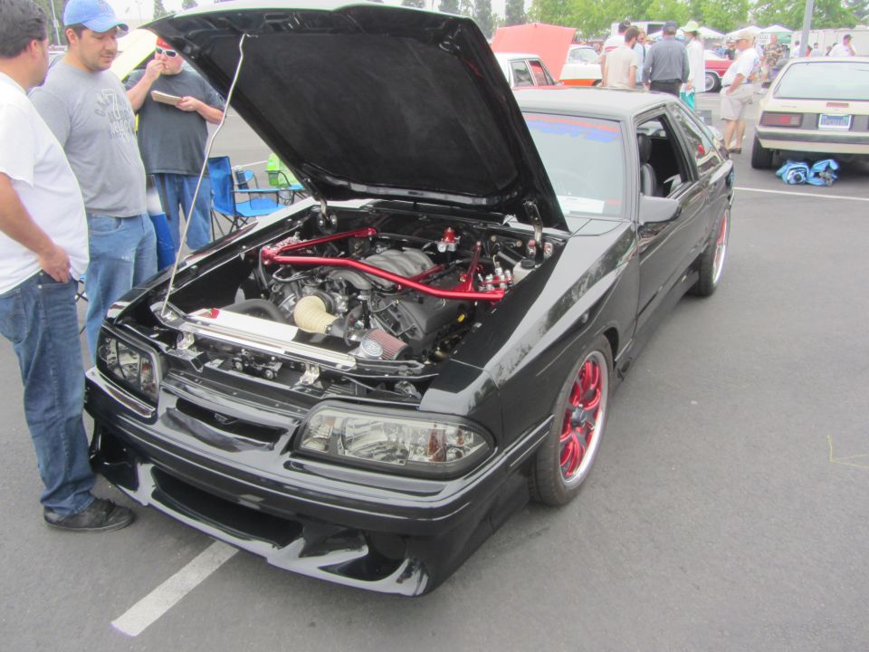 Black car with red wheels and open hood showing engine, parked outdoors