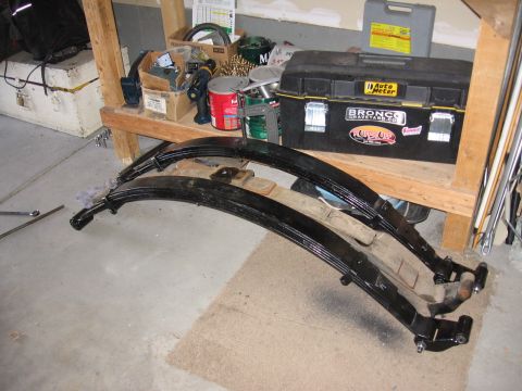 1995 Ford Bronco - Leaf springs are laid out on the floor, with a toolbox and various automotive parts visible on a shelf in the background.