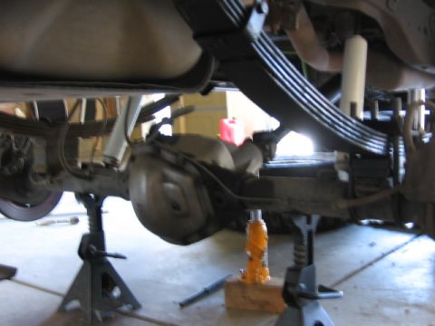1995 Ford Bronco - The rear axle and leaf springs of a vehicle are supported by jack stands and a bottle jack.