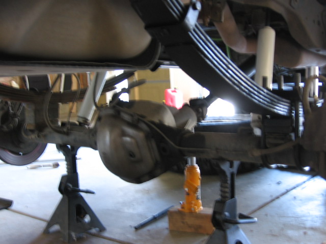 Truck rear axle and leaf spring pack on jack stands with an orange bottle jack