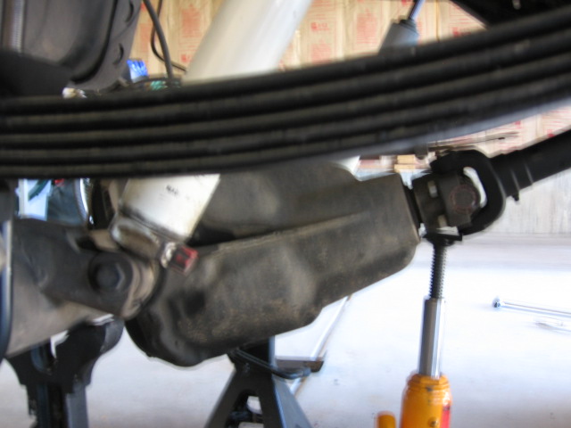 Black multi-leaf spring pack and white shock over a rear axle supported by jack stands
