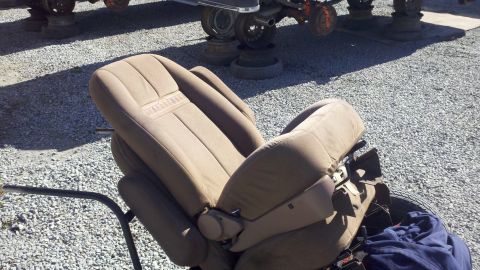 1978 Ford Bronco - A tan car seat with "BRONCO" embossed on the headrest is shown in a junkyard.