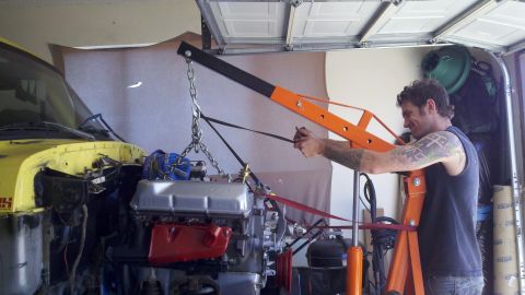 1978 Ford Bronco - A man is using an engine hoist to remove an engine from a vehicle in a garage.