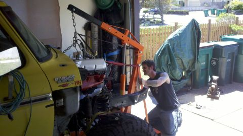 1978 Ford Bronco - A man works on removing the engine from a yellow 1978 Ford Bronco in a garage.