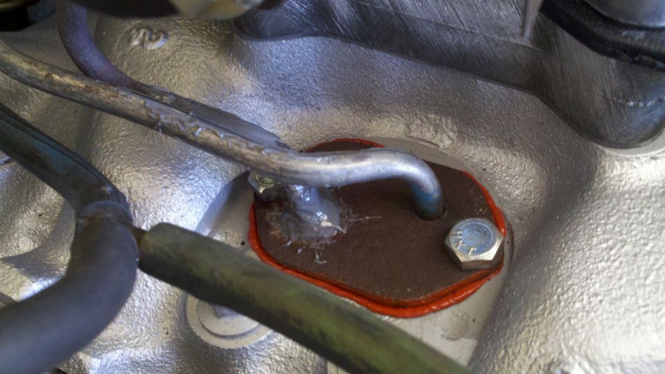 Engine component with a brown gasket secured by a bolt, metal lines nearby