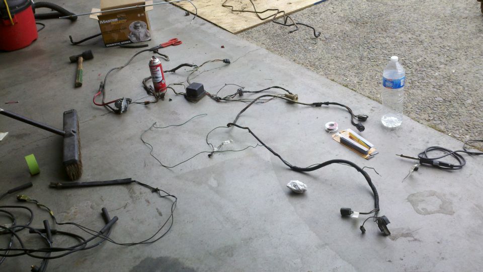 Vehicle wiring harness laid out on concrete floor with tools and a can of spray lubricant