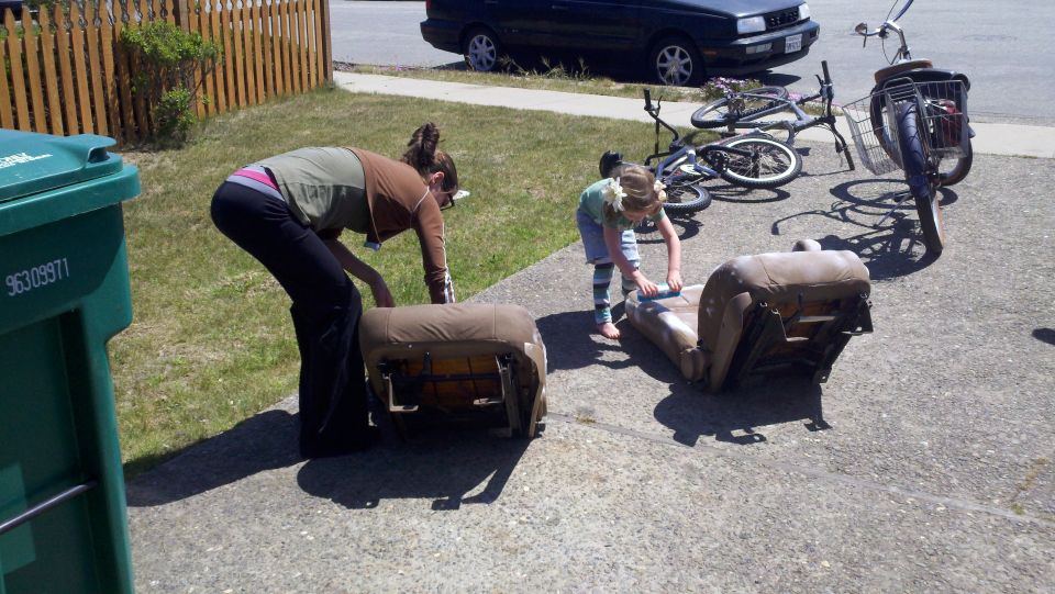 Two car seats on a driveway with people and bicycles nearby