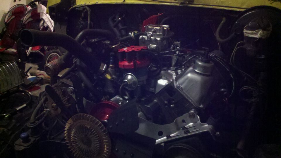 Engine bay with V8 engine, carburetor, and distributor visible. Some parts are red and chrome