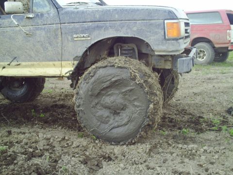 1990 Ford Bronco - A muddy 1990 Ford Bronco is stuck in the mud, with another Bronco visible in the background.