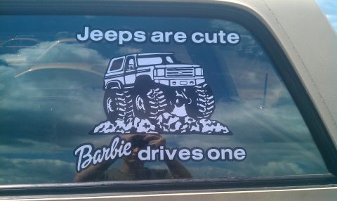 1987 Ford Bronco - A sticker on a vehicle window reads "Jeeps are cute" and "Barbie drives one", a monster truck graphic.