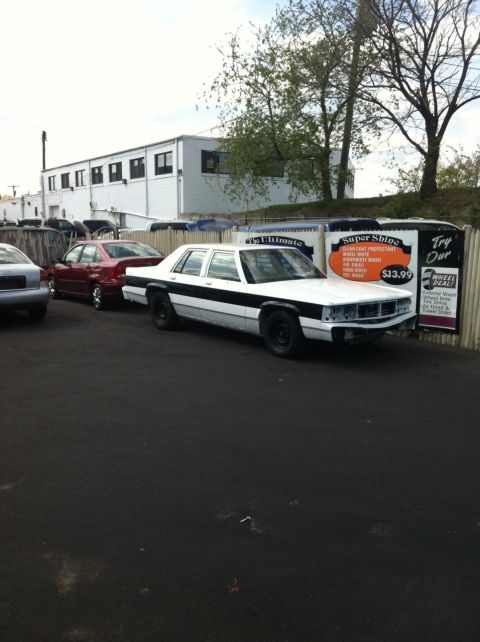 1991 Ford LTD Crown Victoria - This white and black sedan, possibly a 1991 Ford Crown Victoria LTD, is seen from the front 3/4 angle with its front bumper removed.